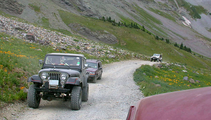 A convoy of off-road vehicles driving on a mountain trail.